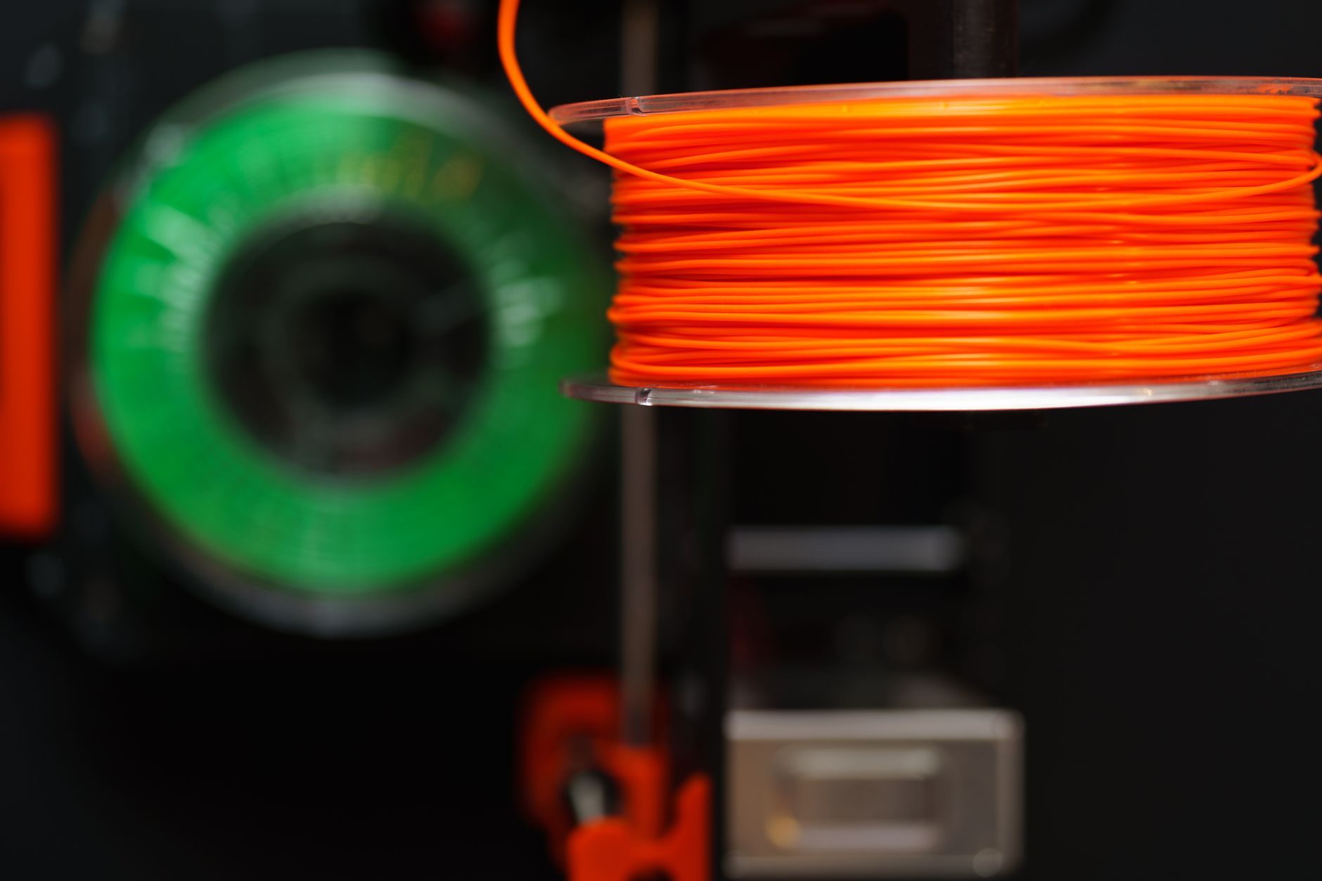 Vibrant orange and green 3D printer filament spools for innovative manufacturing uses.