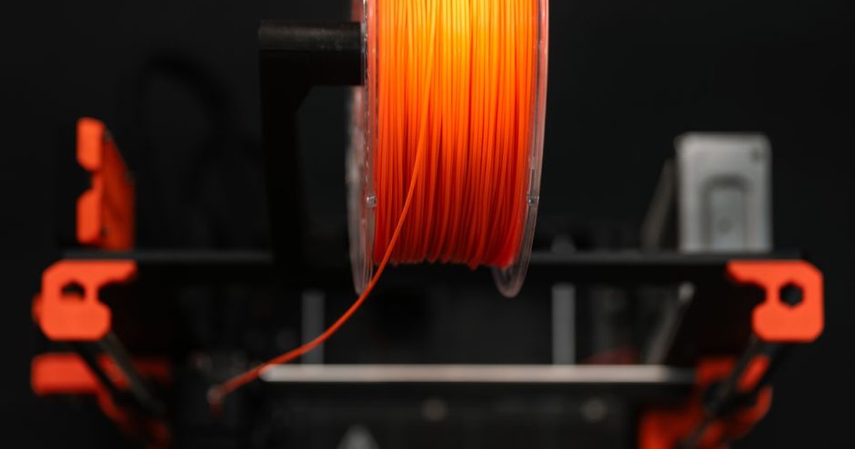 Close-up of an orange 3D printer filament spool in a workshop setting, highlighting innovation and design.