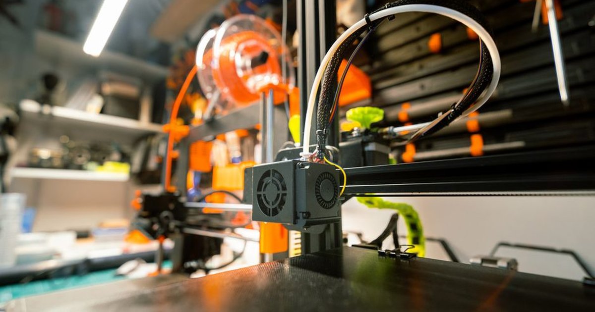 Close-up of a 3D printer in a workshop with visible tools and spool.