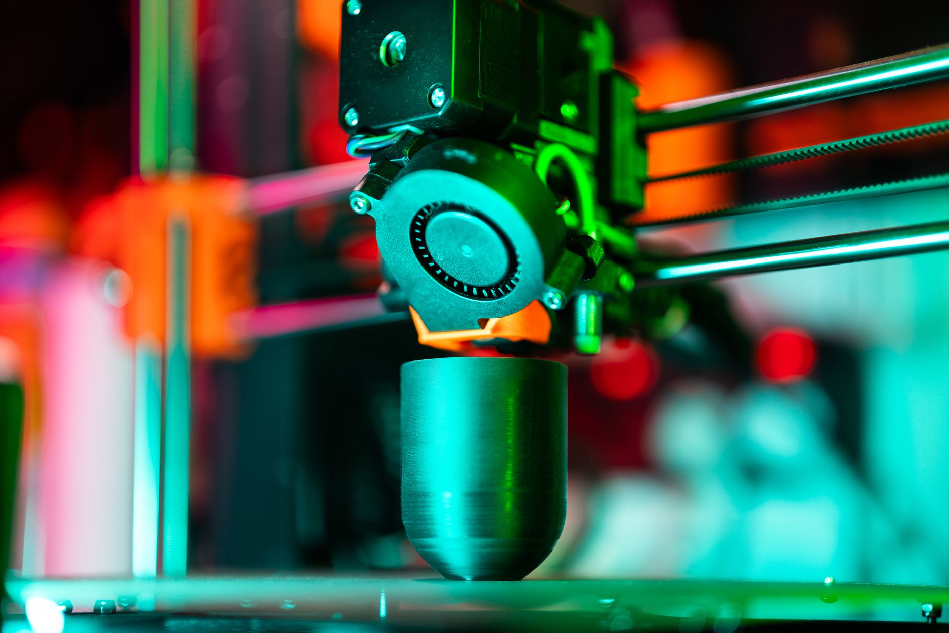 Detailed view of a 3D printer in action, extruding orange plastic components.