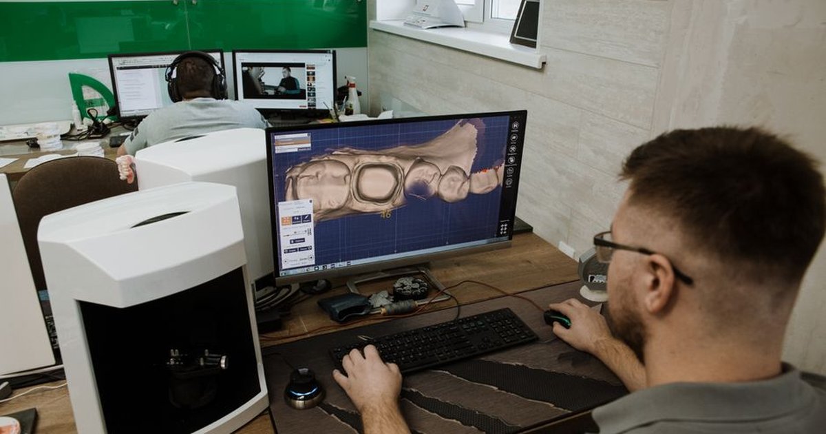 Back view of anonymous male programmer sitting at table and creating 3d model of teeth while working in modern dental laboratory